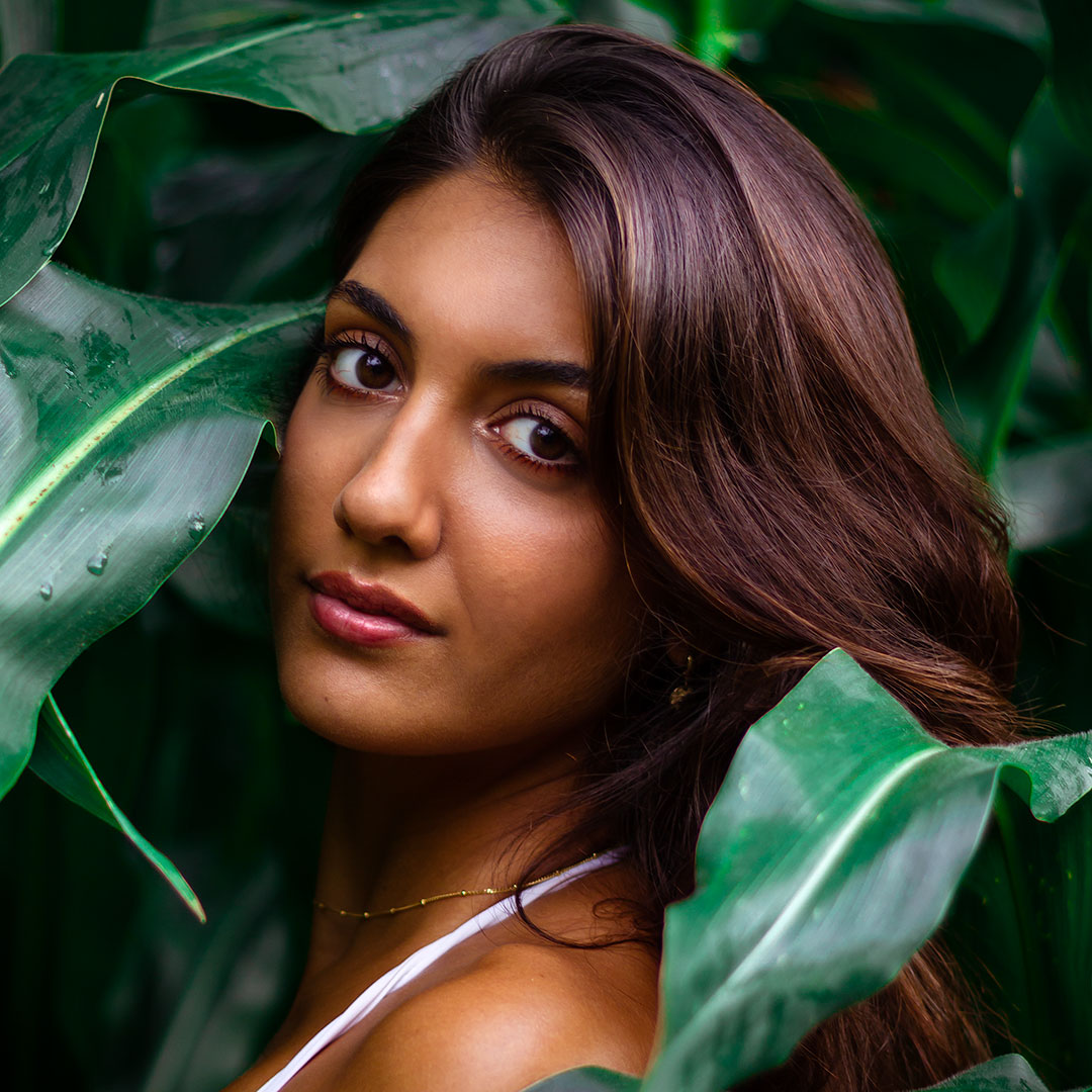 Junge Frau zwischen großen Pflanzenblättern bei einem Portrait Fotoshooting