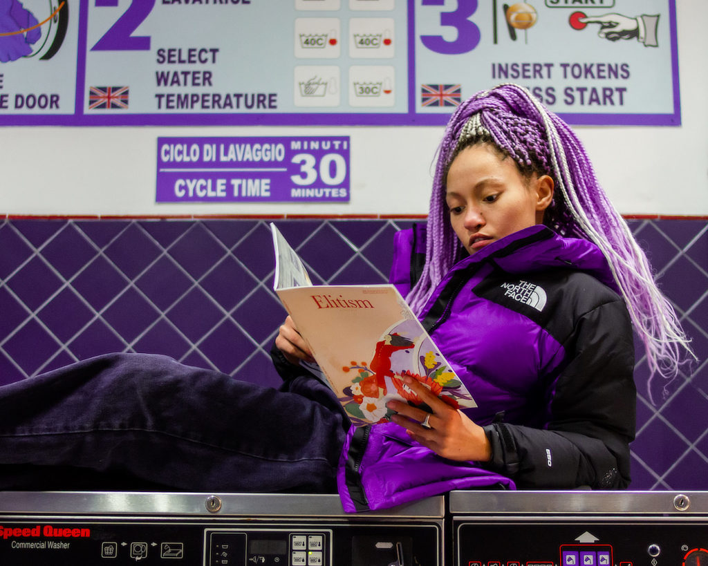 Frau liest in einem Waschsalon mit lila Jacke von The North Face bei einem Fotoshooting für Social Media