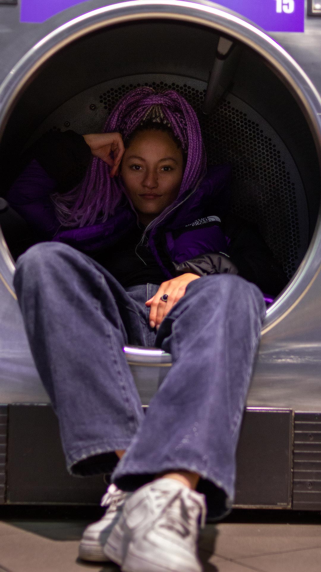 Frau sitzt in einer Waschmaschine mit lila Jacke von The North Face bei einem Fotoshooting für Social Media