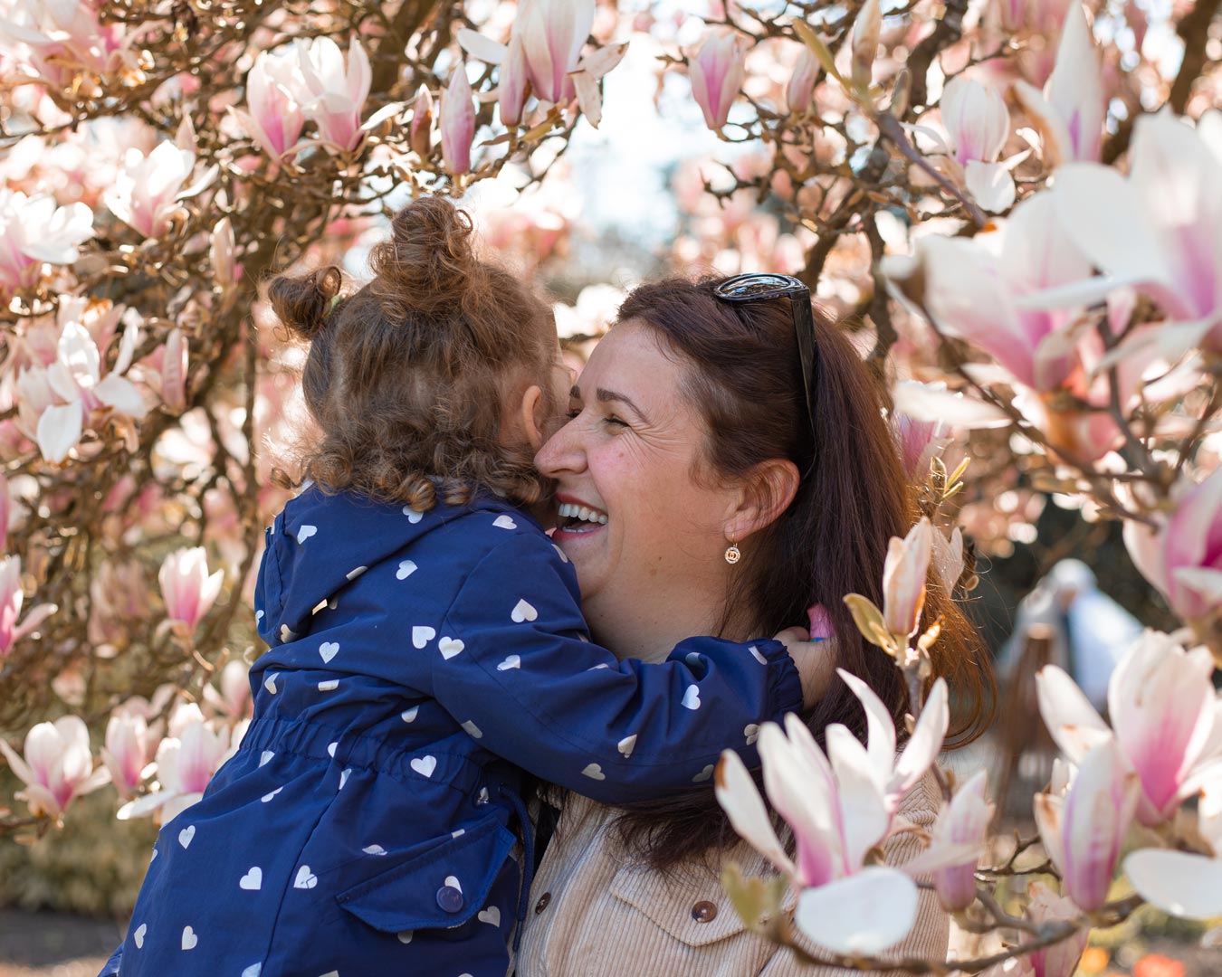 Portrait Familie Mutter lacht mit ihrer Tochter im Arm umgeben von Magnolien