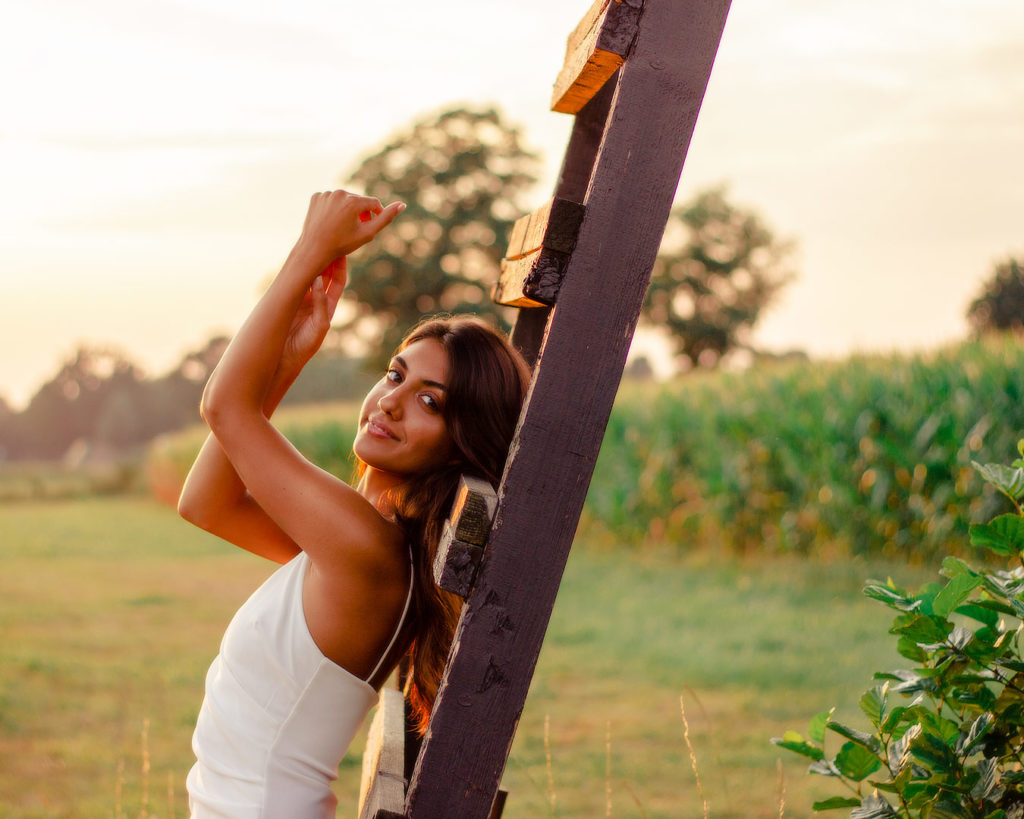 Portraitfoto einer junge Frau im weißen Kleid an einer Holzleiter gelehnt