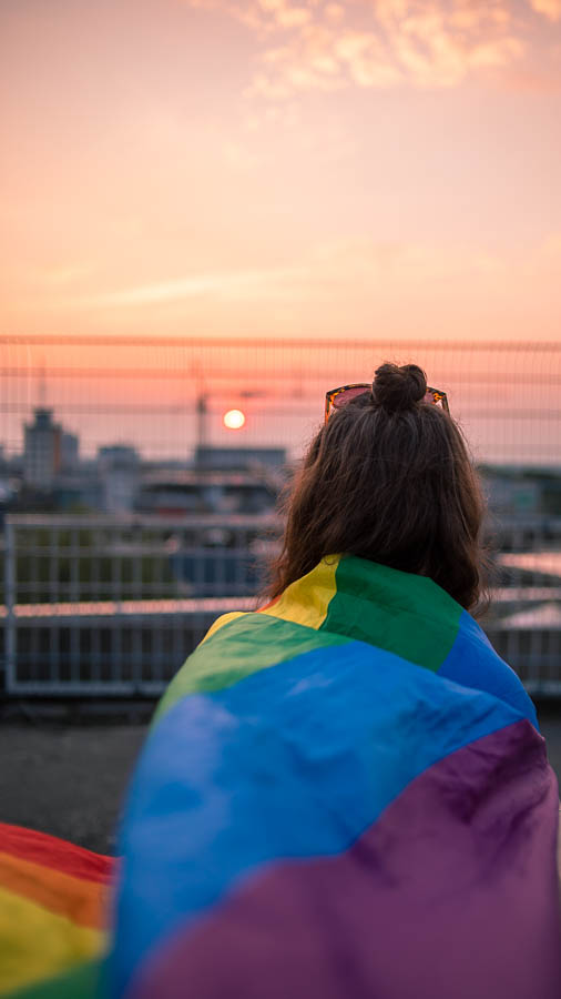 junge Frau mit Pride Regenbogenflagge mit Sonnenuntergang im Hintergrund