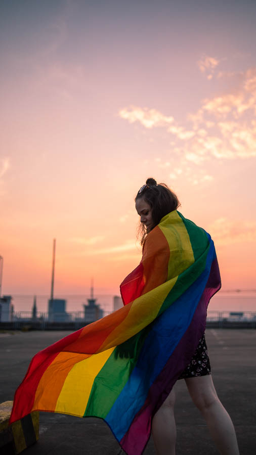 junge Frau mit Pride Regenbogenflagge mit Sonnenuntergang im Hintergrund