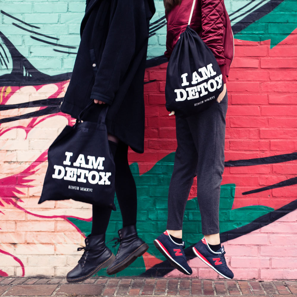 Commercial Produktfoto zwei Frauen springen hoch und tragen je einen Beutel mit der Aufschrift I AM DETOX