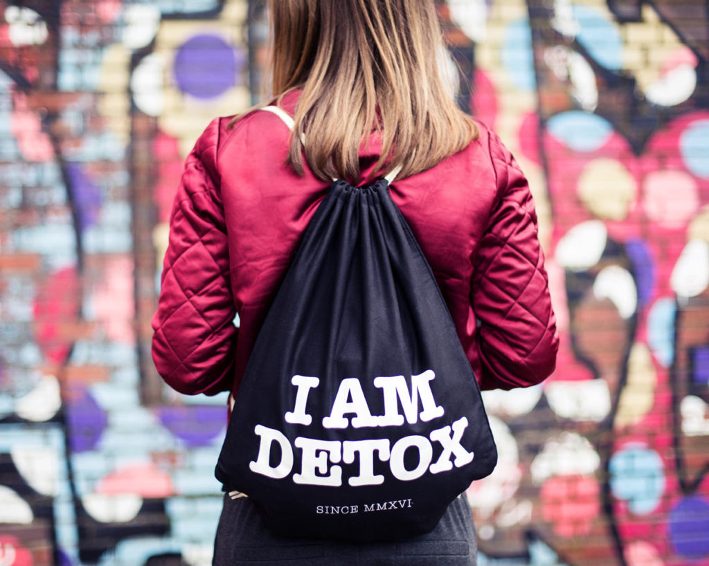 Commercial Produktfoto Frau mit roter Jacke trägt einen Beutel mit der Aufschrift I AM DETOX