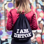 Commercial Produktfoto Frau mit roter Jacke trägt einen Beutel mit der Aufschrift I AM DETOX