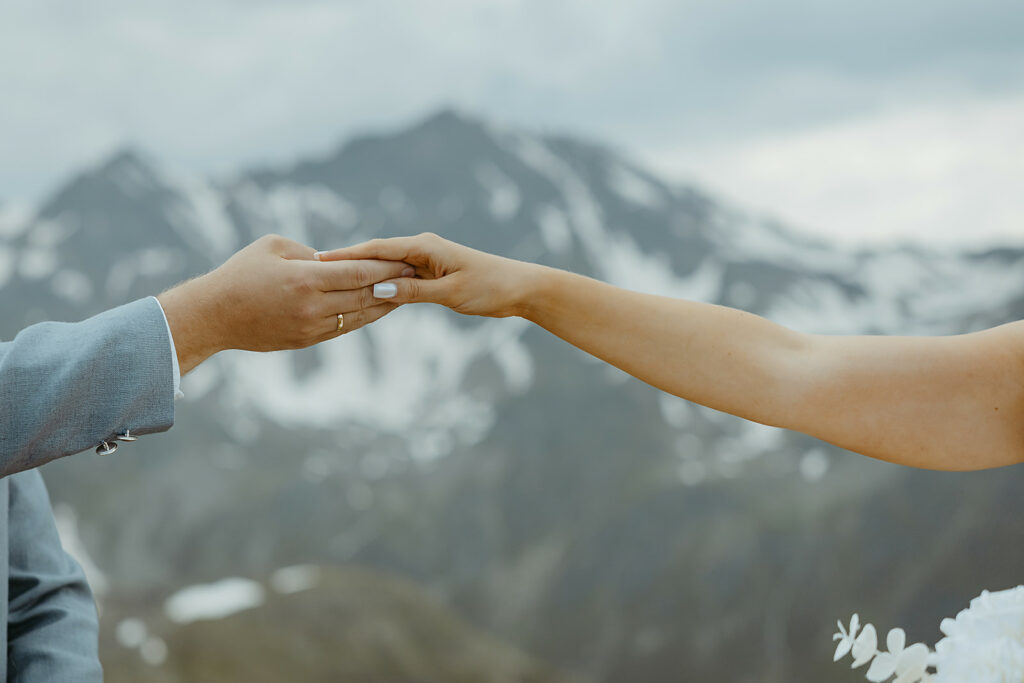 Hochzeitsfoto Elopement Micro Wedding in den Bergen Braut und Bräutigam halten ihre Hände sacht im Hintergrund sind die Berge