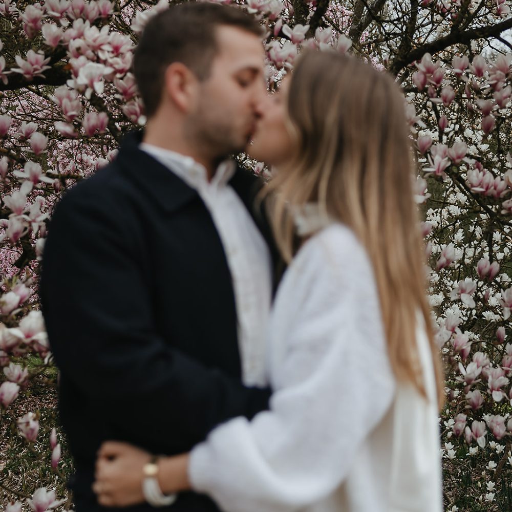 Verlobungsfoto Paar steht vor einer Magnolie und küsst sich